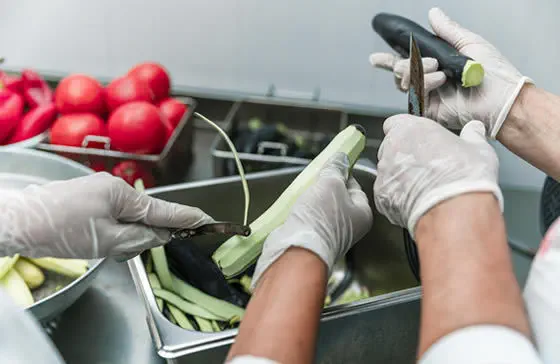 Manos con guantes cortando verduras en una cocina profesional